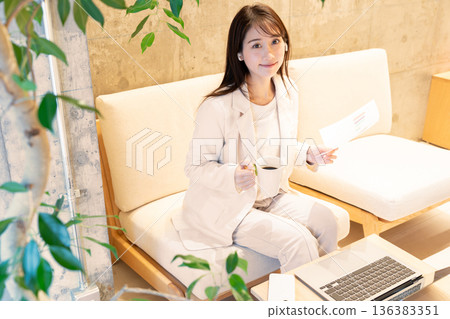 A young woman sitting on a sofa in a cafe and having a remote meeting on a computer A young woman sitting on a sofa in a cafe and having a remote meeting on a computer 136383351