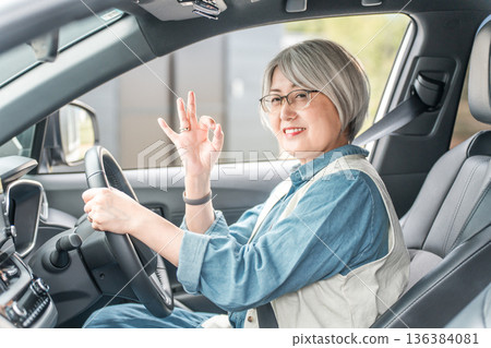 Smiling elderly female driver giving an OK sign in the driver's seat of a car Smiling elderly female driver giving an OK sign in the driver's seat of a car 136384081