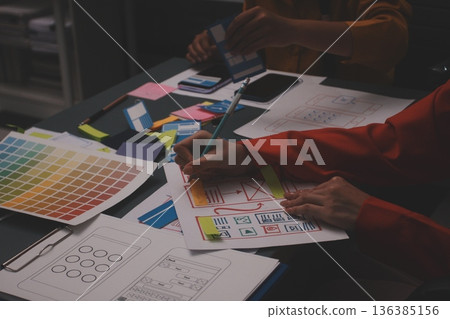 Team of uxui designers pointing at computer screen, discussing new mobile app design in the office Team of uxui designers pointing at computer screen, discussing new mobile app design in the office 136385156