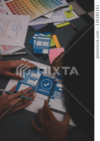 Team of uxui designers pointing at computer screen, discussing new mobile app design in the office 136385161