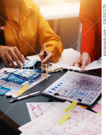 Team of uxui designers pointing at computer screen, discussing new mobile app design in the office 136385176