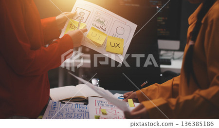 Team of uxui designers pointing at computer screen, discussing new mobile app design in the office Team of uxui designers pointing at computer screen, discussing new mobile app design in the office 136385186