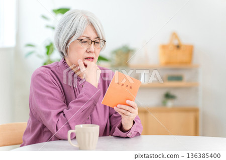 一位憂心忡忡的老婦人在家看著她的退休金手冊 136385400