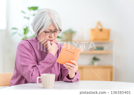 一位憂心忡忡的老婦人在家看著她的退休金手冊 136385401