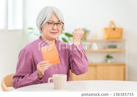 一位頭髮花白的老婦人拿著一本退休金手冊。 136385735