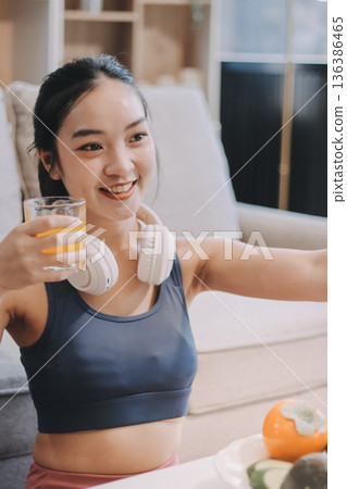 Fit young Asian women in activewear sitting on yoga mat and eating fresh vegetable salad after workout, representing clean eating, fitness lifestyle, wellness routine and health balance. 136386465