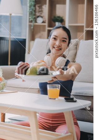 Fit young Asian women in activewear sitting on yoga mat and eating fresh vegetable salad after workout, representing clean eating, fitness lifestyle, wellness routine and health balance. 136386466