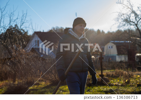Caucasian man farm worker or gardener walks with shovel through garden. Farmer concept for organic gardening and agriculture in spring or autumn. 136386713