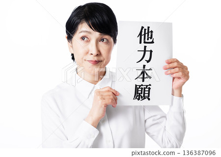 一位身穿白襯衫的老婦人雙手拿著一張寫著「tariki hongan」字樣的紙,目光移向別處。 一位身穿白襯衫的老婦人雙手拿著一張寫著「tariki hongan」字樣的紙,目光移向別處。 136387096
