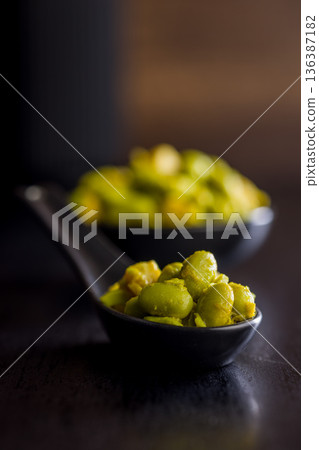 Fresh salad with edamame beans on ceramic spoon on black table. 136387182
