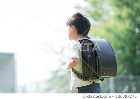 A boy (boy) running with a school bag on his back in the schoolyard with the school building and greenery in the background. No face, an image of the future and hope. A boy (boy) running with a school bag on his back in the schoolyard with the school building and greenery in the background. No face, an image of the future and hope. 136387276