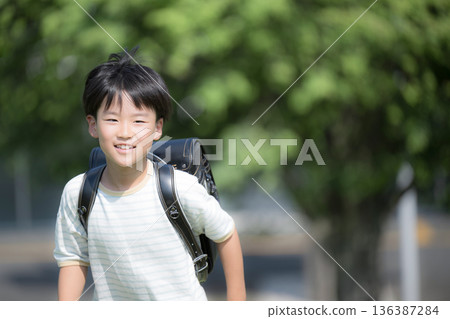 Close-up of a smiling boy (male) running with a school bag on his back in the schoolyard with the school building and greenery in the background Close-up of a smiling boy (male) running with a school bag on his back in the schoolyard with the school building and greenery in the background 136387284