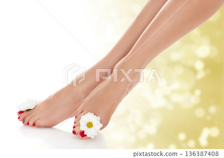 Beautiful female legs with daisy flower on golden blurred background. 136387408