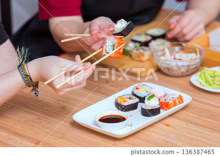 Close up of female hands holding chopsticks and eating sushi rolls Close up of female hands holding chopsticks and eating sushi rolls 136387465
