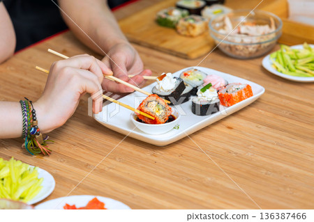 Close up of female hands holding chopsticks and eating sushi rolls. Close up of female hands holding chopsticks and eating sushi rolls. 136387466