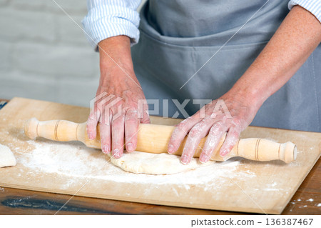 Chef rolling dough for pizza on a wooden table, female hands with rolling pin Chef rolling dough for pizza on a wooden table, female hands with rolling pin 136387467