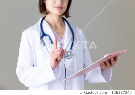A middle-aged female doctor in a white coat pointing up 136387843