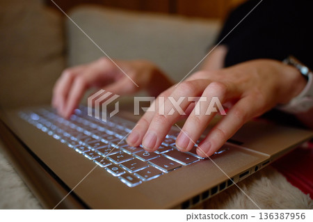 Close up of hands typing on laptop keyboard while sitting on sofa. Concept of remote work 136387956