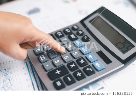 Close-up of a hand pressing calculator keys for budgeting, accounting and financial analysis. Business expense planning, tax calculation, office desk background, copy space for paperwork. Close-up of a hand pressing calculator keys for budgeting, accounting and financial analysis. Business expense planning, tax calculation, office desk background, copy space for paperwork. 136388135