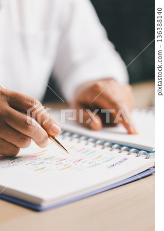 Hand writing notes in a notebook beside a calculator on office desk for budgeting and accounting. Personal finance planning, expense tracking, tax calculation, soft focus background, copy space. Hand writing notes in a notebook beside a calculator on office desk for budgeting and accounting. Personal finance planning, expense tracking, tax calculation, soft focus background, copy space. 136388140