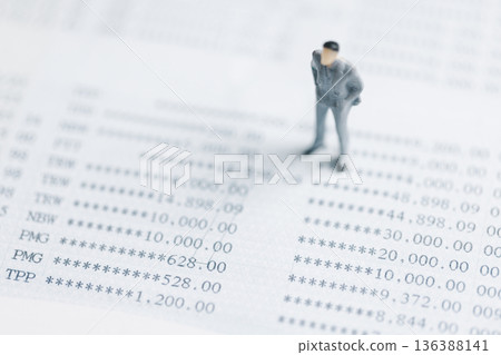 Miniature businessman standing on financial statement numbers, reviewing accounts and audit results. Concept of accounting, tax, risk management and budget control with copy space, soft focus. 136388141