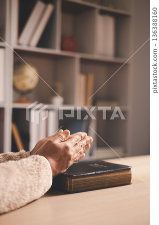 Clasped hands in prayer over an open book, warm light and shallow depth of field, symbolizing faith, devotion, reflection and hope for spiritual guidance during quiet study at home. Clasped hands in prayer over an open book, warm light and shallow depth of field, symbolizing faith, devotion, reflection and hope for spiritual guidance during quiet study at home. 136388160