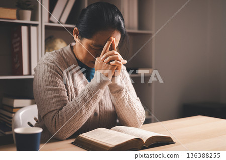 Stressed woman with hand on face beside an open Bible and glasses on a desk, warm indoor light and copy space, expressing grief, prayer, faith and seeking comfort during quiet reflection at home. Stressed woman with hand on face beside an open Bible and glasses on a desk, warm indoor light and copy space, expressing grief, prayer, faith and seeking comfort during quiet reflection at home. 136388255