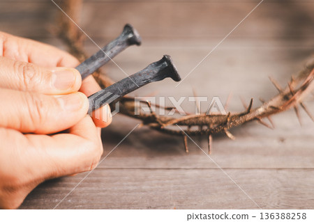 Hand offering an iron nail and crown of thorns on dark background, dramatic light with copy space, symbolizing crucifixion, sacrifice, Good Friday, Holy Week and Easter faith for believers worldwide. Hand offering an iron nail and crown of thorns on dark background, dramatic light with copy space, symbolizing crucifixion, sacrifice, Good Friday, Holy Week and Easter faith for believers worldwide. 136388258