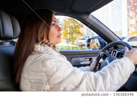 woman with long brown hair driver in a modern car. woman looks ahead at the road. Safe driving behavior and road trip. delivery, women's taxi 136388346