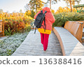Woman walking on wooden boardwalk with backpack in autumn park. Hiking for health and wellness. Active lifestyle for overweight. 136388416