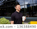 Happy Caucasian man holding coffee cup outdoors. Businessman enjoying a coffee break. Daily city life and professional lifestyle concept. 136388490