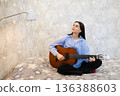 actress, singer, influencer, blogger. Woman playing acoustic guitar while sitting on bed, looking up thoughtfully with sparkling wall decorations, musical inspiration and dream 136388603