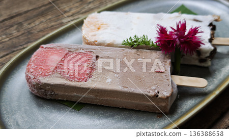 Dark chocolate ice cream with coconut milk, fresh strawberry and strawberry jam, served on a stick. 136388658