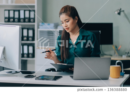 Determined asian businesswoman works late in a modern office, confidently analyzing data on her laptop, embodying success and professionalism with a smile Determined asian businesswoman works late in a modern office, confidently analyzing data on her laptop, embodying success and professionalism with a smile 136388880