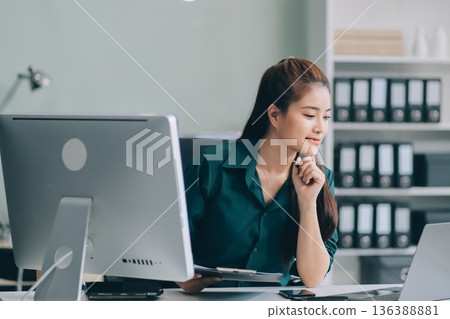 Determined asian businesswoman works late in a modern office, confidently analyzing data on her laptop, embodying success and professionalism with a smile Determined asian businesswoman works late in a modern office, confidently analyzing data on her laptop, embodying success and professionalism with a smile 136388881