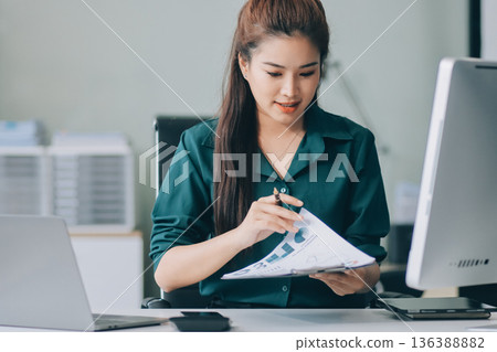 Determined asian businesswoman works late in a modern office, confidently analyzing data on her laptop, embodying success and professionalism with a smile Determined asian businesswoman works late in a modern office, confidently analyzing data on her laptop, embodying success and professionalism with a smile 136388882