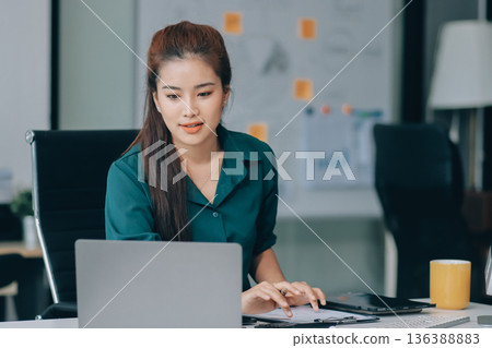 Determined asian businesswoman works late in a modern office, confidently analyzing data on her laptop, embodying success and professionalism with a smile Determined asian businesswoman works late in a modern office, confidently analyzing data on her laptop, embodying success and professionalism with a smile 136388883