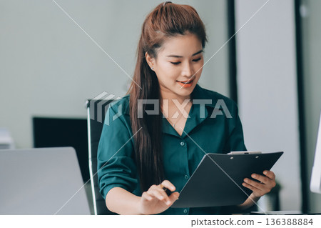 Determined asian businesswoman works late in a modern office, confidently analyzing data on her laptop, embodying success and professionalism with a smile Determined asian businesswoman works late in a modern office, confidently analyzing data on her laptop, embodying success and professionalism with a smile 136388884