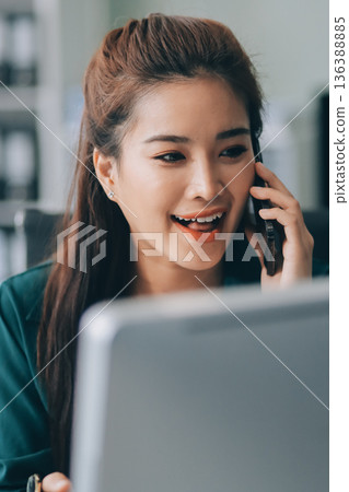 Determined asian businesswoman works late in a modern office, confidently analyzing data on her laptop, embodying success and professionalism with a smile 136388885