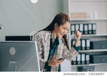 Determined asian businesswoman works late in a modern office, confidently analyzing data on her laptop, embodying success and professionalism with a smile Determined asian businesswoman works late in a modern office, confidently analyzing data on her laptop, embodying success and professionalism with a smile 136388897
