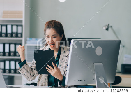 Determined asian businesswoman works late in a modern office, confidently analyzing data on her laptop, embodying success and professionalism with a smile 136388899