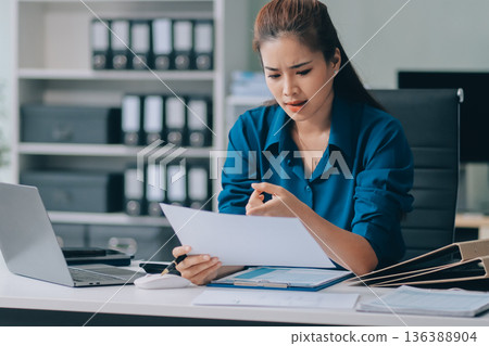 Young businesswoman is holding two credit cards with a worried expression, trying to decide which one to use to pay off her debt 136388904