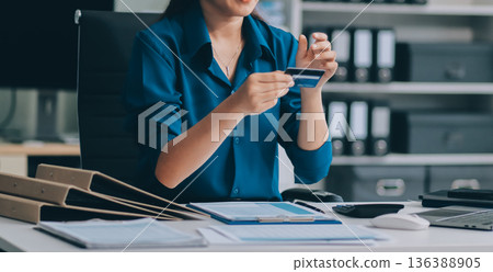 Young businesswoman is holding two credit cards with a worried expression, trying to decide which one to use to pay off her debt Young businesswoman is holding two credit cards with a worried expression, trying to decide which one to use to pay off her debt 136388905