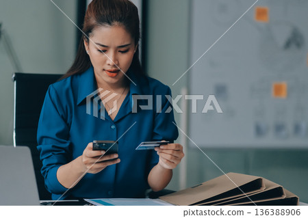 Young businesswoman is holding two credit cards with a worried expression, trying to decide which one to use to pay off her debt Young businesswoman is holding two credit cards with a worried expression, trying to decide which one to use to pay off her debt 136388906