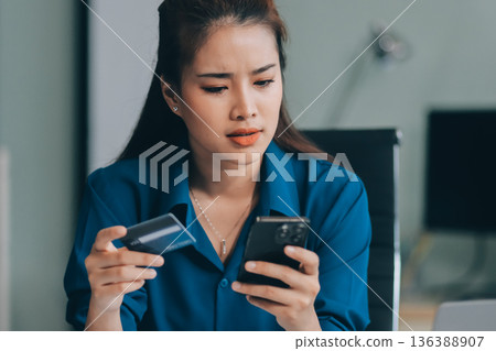 Young businesswoman is holding two credit cards with a worried expression, trying to decide which one to use to pay off her debt Young businesswoman is holding two credit cards with a worried expression, trying to decide which one to use to pay off her debt 136388907