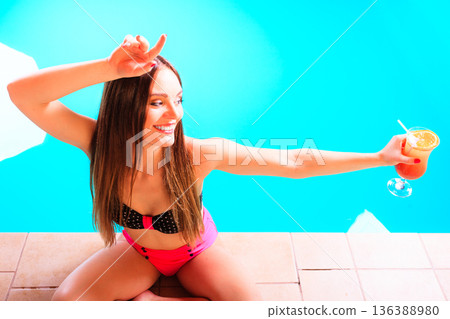 Woman with cocktail drink at swimming pool edge. Woman with cocktail drink at swimming pool edge. 136388980