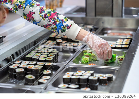 Buying sushi rolls in a store. A customer's hand in a disposable glove selects sushi rolls in a store. Buying sushi rolls in a store. A customer's hand in a disposable glove selects sushi rolls in a store. 136389264