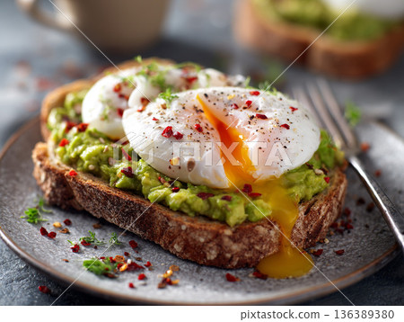 Enjoying a slice of sourdough toast with mashed avocado and poached eggs for breakfast in a bright kitchen 136389380