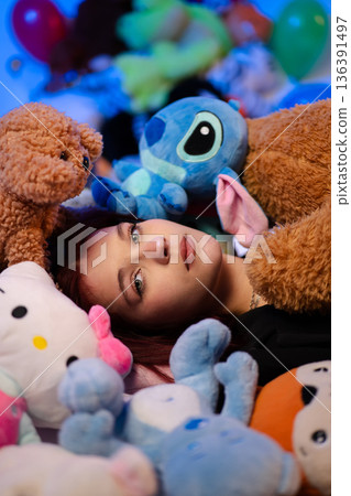 A young woman lies on the floor surrounded by many plush toys. 136391497