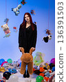 The woman stands surrounded by toys and balloons in a studio room. 136391503